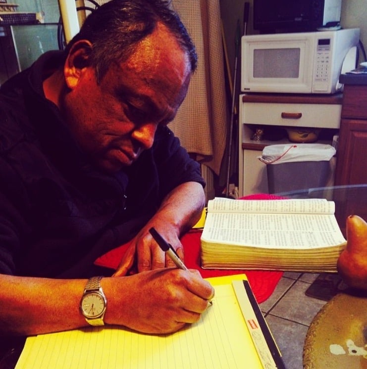 Pastor del Concilio Internacional Visión en Acción estudiando la Biblia y escribiendo notas en un block amarillo, en su momento devocional de preparación, en una fotografía de tonos antiguos
