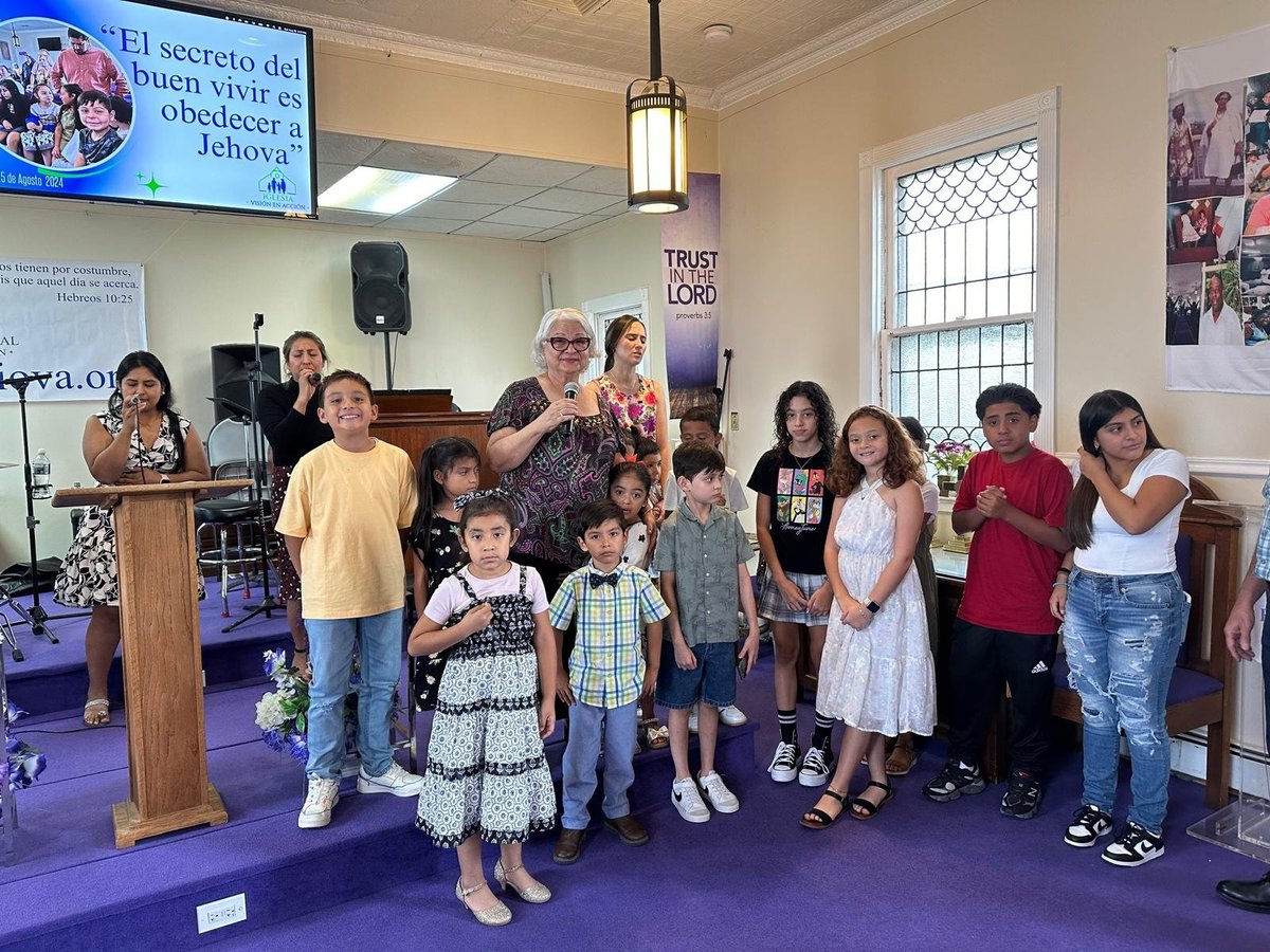 Grupo de niños y adultos de la congregación del Concilio Internacional Visión en Acción reunidos en el escenario del templo durante un servicio comunitario